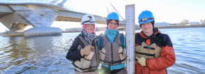 MWMO monitoring team members pose next to a staff gauge in the Mississippi River.