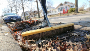 A broom being used to sweep leaves off of a stormdrain.