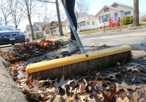 A broom being used to sweep leaves off of a stormdrain.