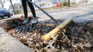 A broom sweeping leaves from a stormdrain.