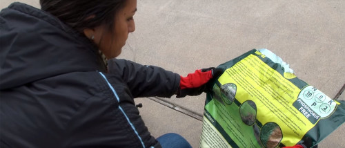 A woman reads instructions on a bag of fertilizer