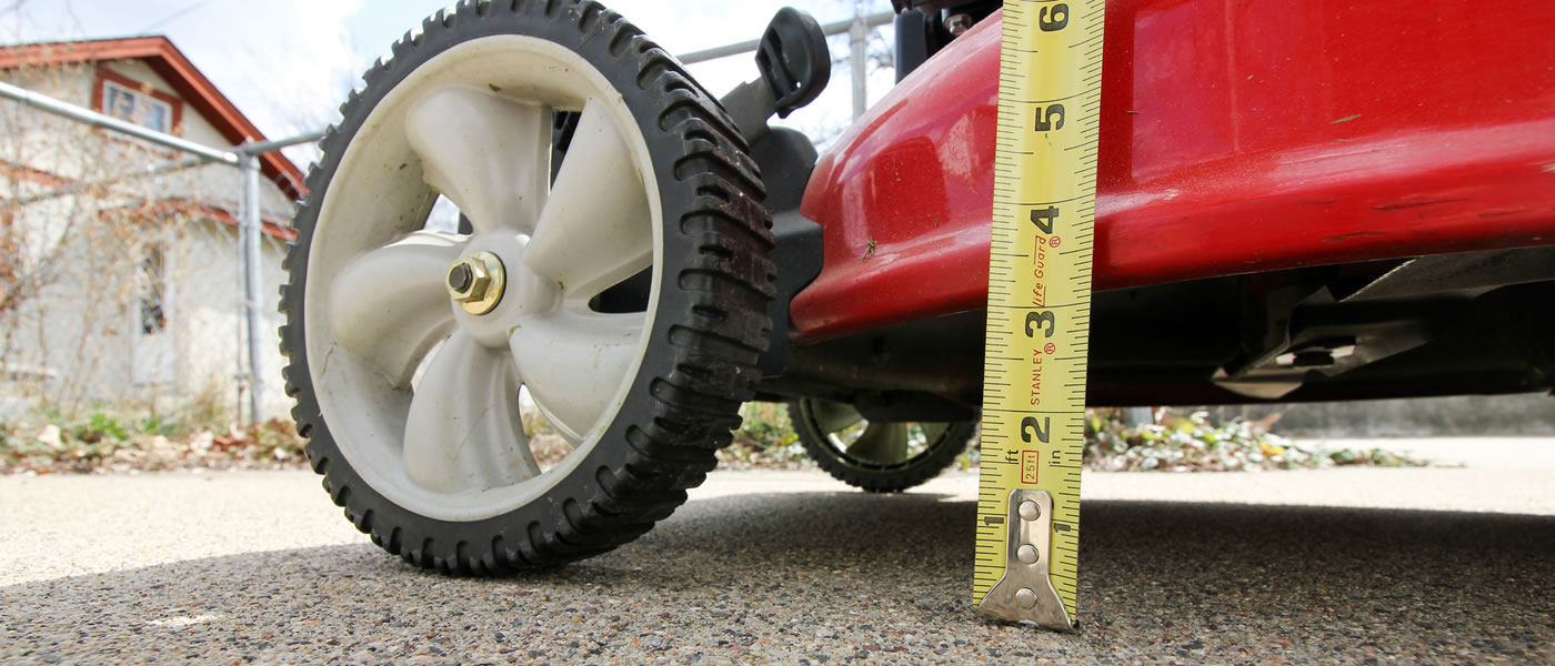 A tape measure is used to check the height on a lawn mower.