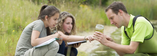 Two students and a teacher examine a water sample.