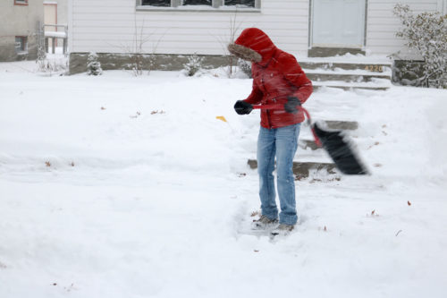 woman in red coat shoveling snow