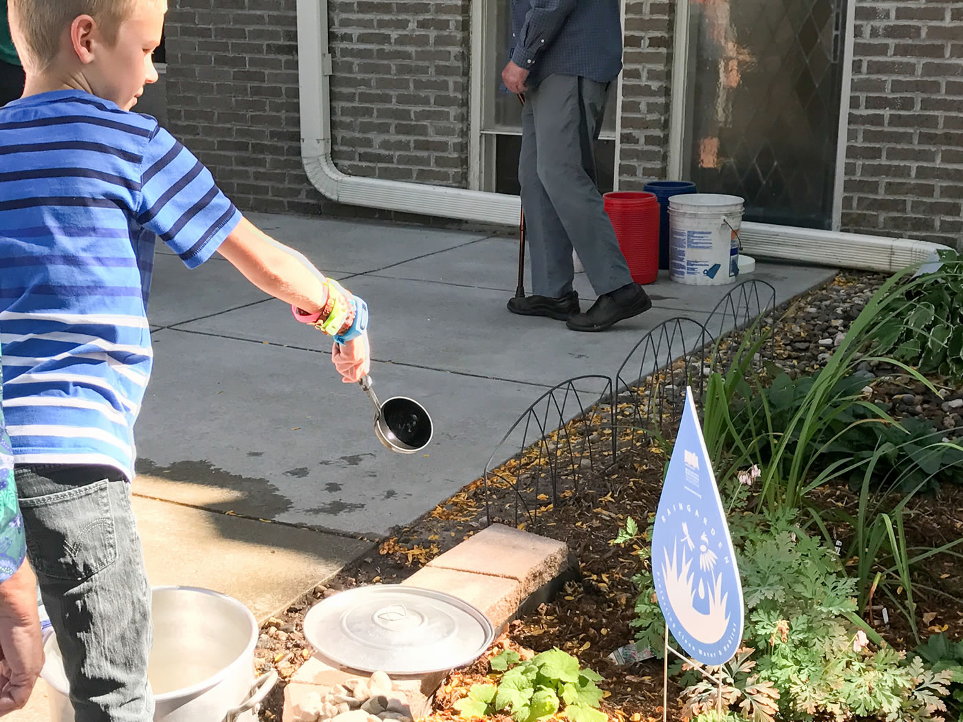 A young church member ladles a spoonful of water onto one of the raingardens.