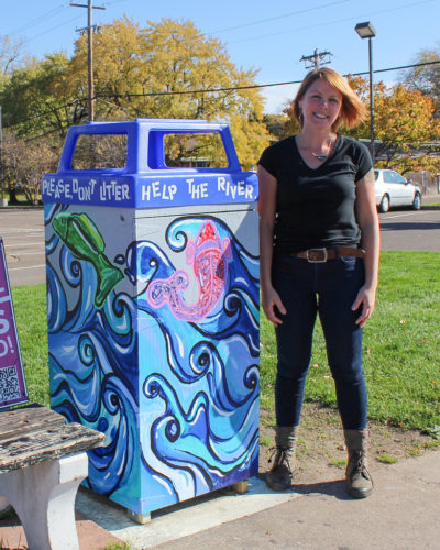 Rebecca Krueger standing next to one of her Trash Can Mural Project creations.