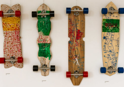 Youth-designed longboards with Mississippi River art hang on a wall at an art gallery.