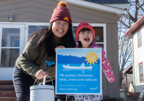 A woman and child hold an Adopt-A-Drain sign.