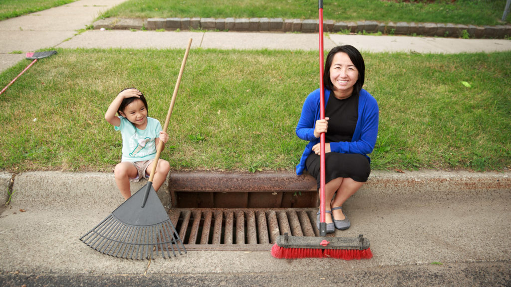 A woman and child sit on a curb next to a cleaned storm grate.