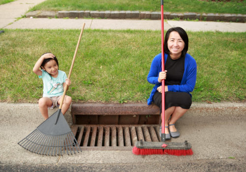 A woman and child sit on a curb next to a cleaned storm grate.