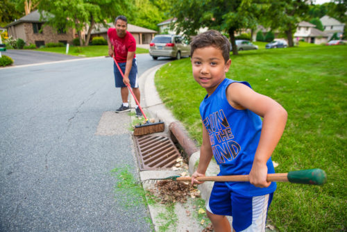 Adult and child sweeping leaves and grass clippings out of a stormdrain.