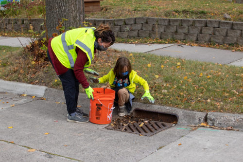 A woman and child picking leaves out of a stormdrain.