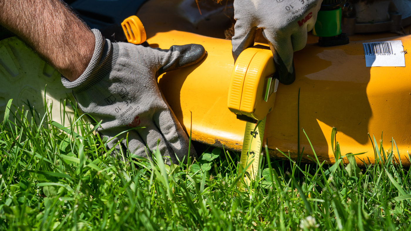 Measuring the height of a lawn mower deck with a tape measure.