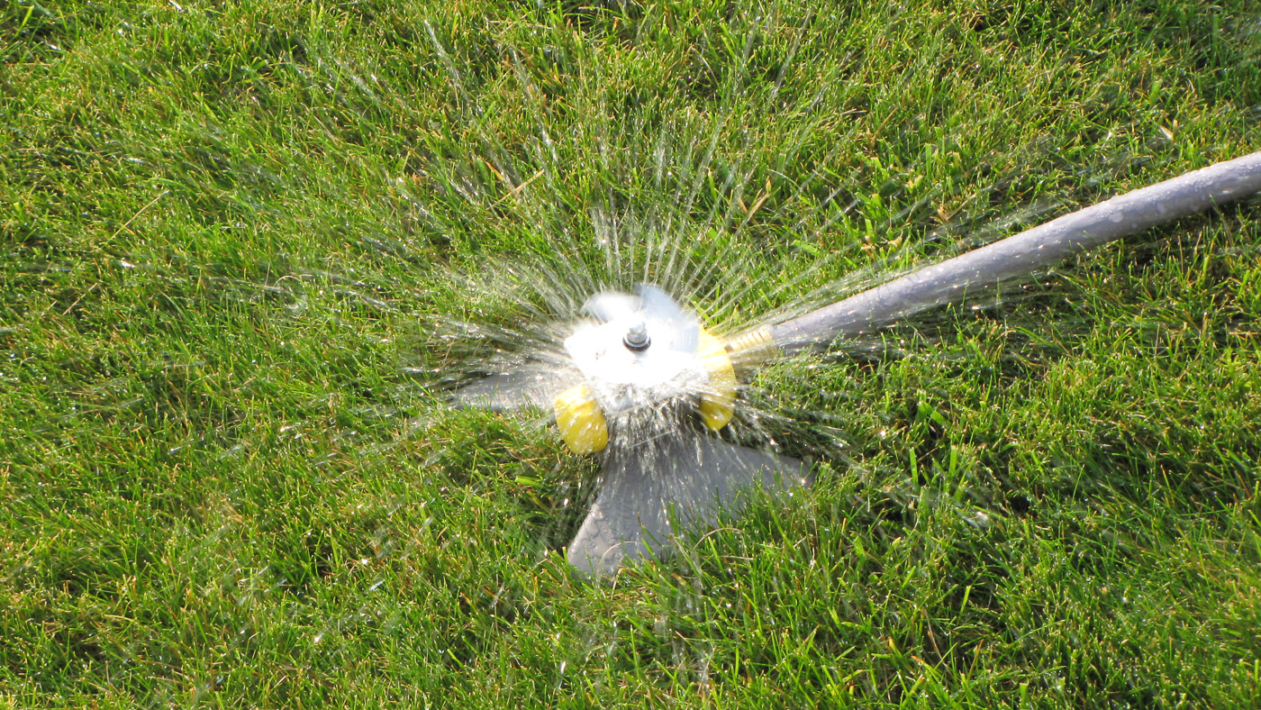 A sprinkler spraying water on a turgrass lawn.