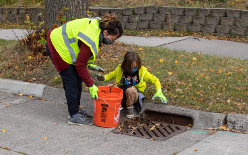 A woman and child removing leaves from a stormdrain.