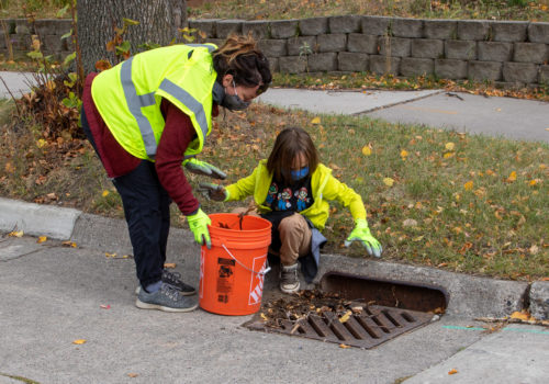 A woman and child removing leaves from a stormdrain.