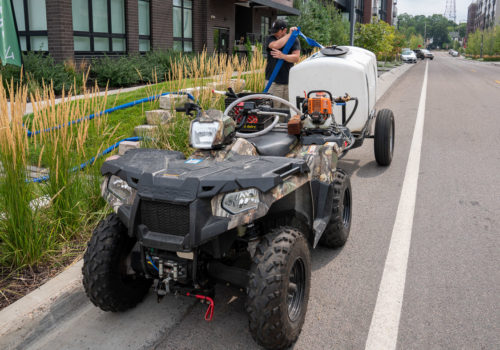 A worker refilling a water tank on the back of an ATV.