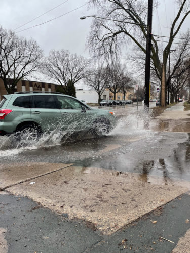 A car drives through a puddle, spraying water in an intersection in Minneapolis.