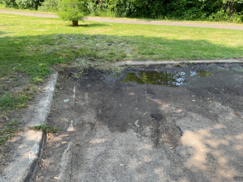 A clogged stormwater inlet at the edge of a parking lot.