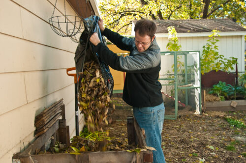 A man dumping leaves into a backyard compost bin.