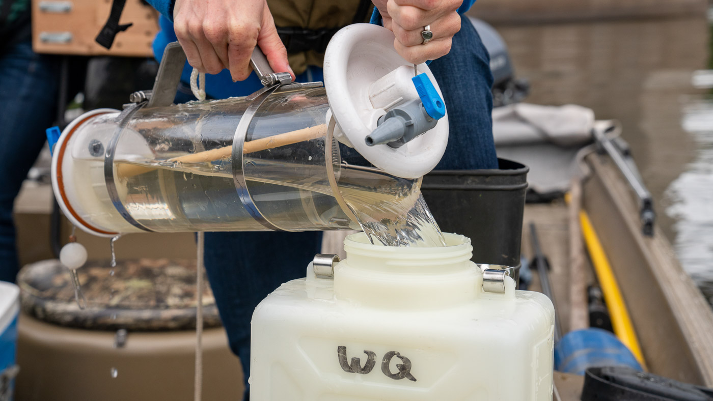 Close-up of a river water sample being poured from a Van Dorn sampler into a container.